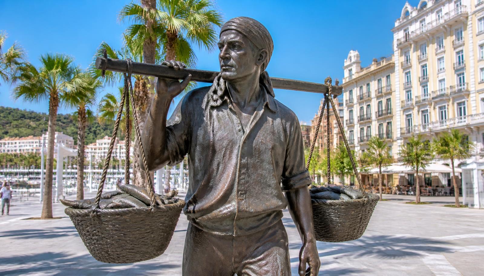 Estatua de bronce del cenachero de Málaga con dos cestos de esparto llenos de pescado sobre el hombro